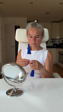 Elegant mature woman trying on long blue tassel earrings in front of a small table mirror.
