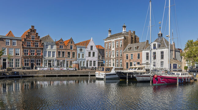 Goes, Netherlands - April 22, 2026: Scenic view of the historic Stadshaven marina with traditional Dutch houses and sailboats reflected in calm water under a clear blue sky.