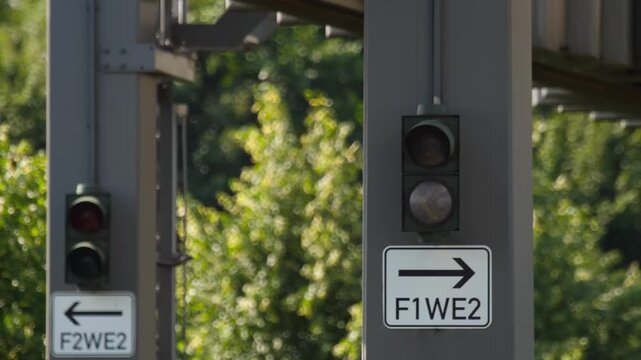 Railway track switch signals displaying red and green lights on grey steel pillars with directional signs in bright daylight, static close-up shot