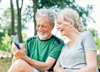 Fototapeta premium Happy active senior couple having fun using smartphone and wearing sportswear, after having an exercise sport activity outdoors