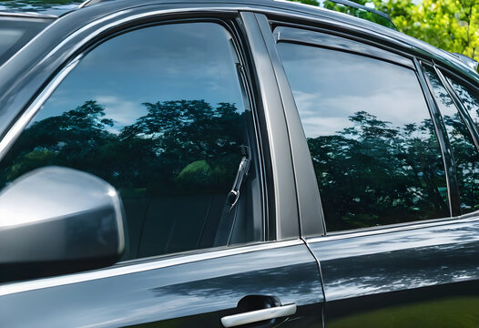 Dark tinted car windows reflecting green trees and blue sky, privacy and sun protection for vehicle interior, the automotive glass offers a sleek exterior detail