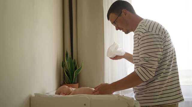 Funny parenthood incident showing a newborn baby boy unexpectedly peeing on his surprised father during a diaper change, capturing a candid and amusing family life moment at home