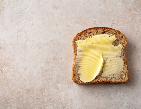 single slice of sourdough with butter melting naturally overhead shot on pale stone surface wide negative space on right