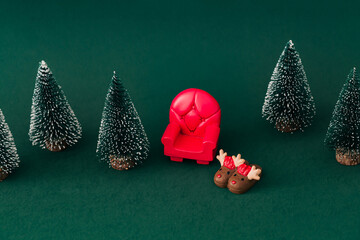 Cozy winter composition with red armchair, reindeer slippers and Christmas trees on green background. Christmas and New Year concept. Creative festive holiday layout. Xmas aesthetic. © Jakov Ilkoski