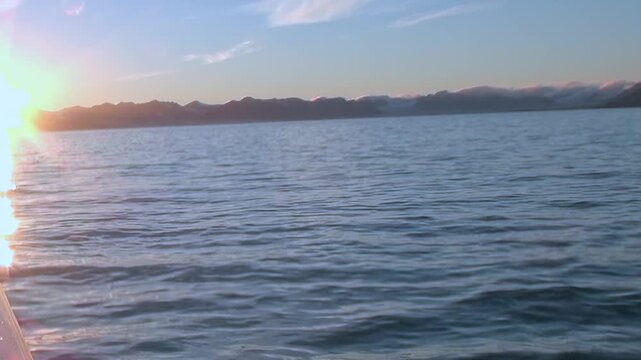 A magnificent Arctic morning unfolds from a ship's deck. Golden rays kiss the rippling surface of the vast Arctic Ocean, painting the waters in hues of light.