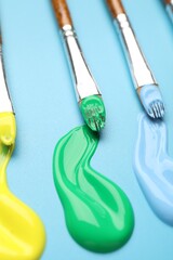 Different brushes with paints on light blue background, closeup © New Africa