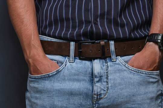 Man posing with both hands in light blue jeans pockets, wearing brown leather belt and striped shirt.