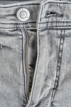 Macro shot grey denim jeans front fly featuring metal button, zipper, and seam details.