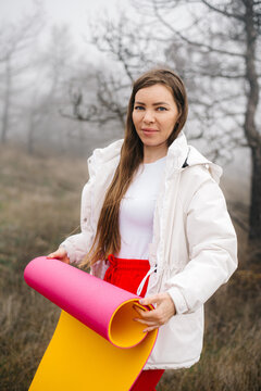 Portrait of a woman holding a rolled yoga mat in a foggy forest