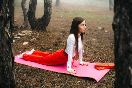Woman meditating in yoga cobra pose framed by tree trunks