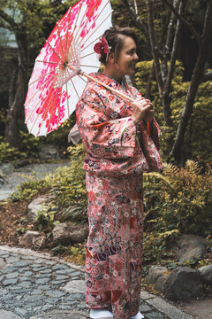 Woman wearing a colorful kimono and holding parasol in a garden in Kyoto Japan