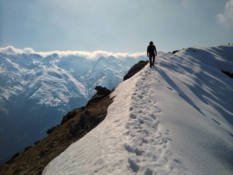 Lone hiker walking along a snowy mountain ridge with panoramic views of the Italian Alps during a winter hike,  Lombardy, Italy.