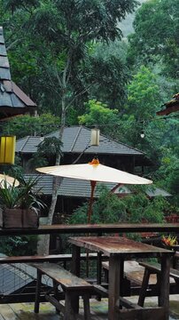 Cozy jungle cafe terrace during tropical rain with peaceful rainforest village atmosphere, Wooden outdoor cafe with lush forest resort in monsoon, slow motion 4k vertical video
