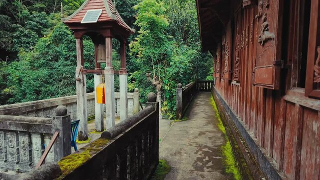 Traditional Buddhist temple bell tower beside historic wooden monastery in tropical forest, Peaceful sacred pathway with carved architecture surrounded by lush greenery and heritage sanctuary 4k