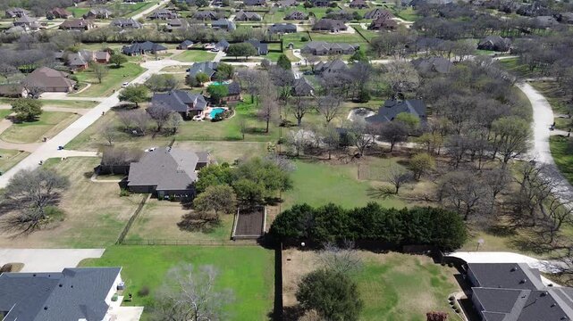 Paved residential lanes skirt Briarhill Estates near dense wooded patches. Aerial drone shot captures side by side executive properties, swimming pools, dark roofs, open lawns, Double Oak, TX