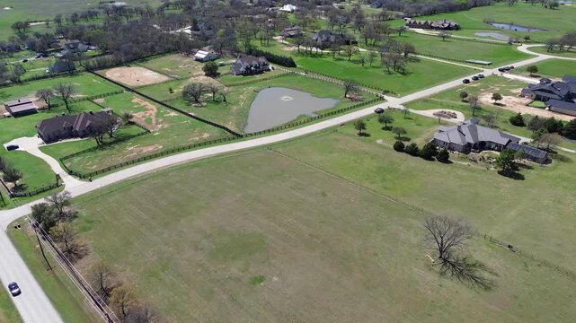 Rural roadways cross Willow Springs Subdivision near vast agricultural fields. Sweeping drone footage illustrates triangular retention pond, split rail fencing, custom manors, Double Oak, TX
