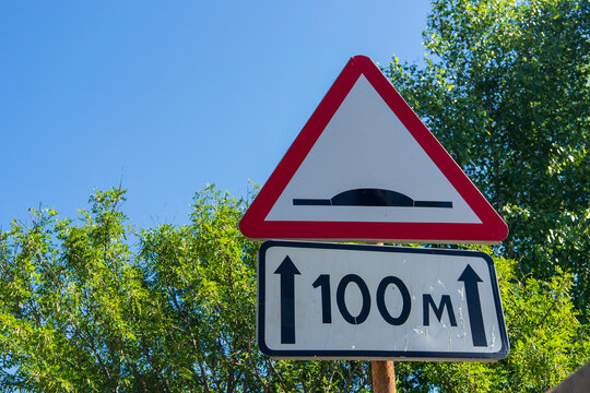 Road warning sign indicating speed bump one hundred meters ahead against blue sky