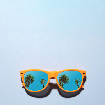 Sunglasses with reflection of tropical palm trees and blue sky on light blue background. Space for text
