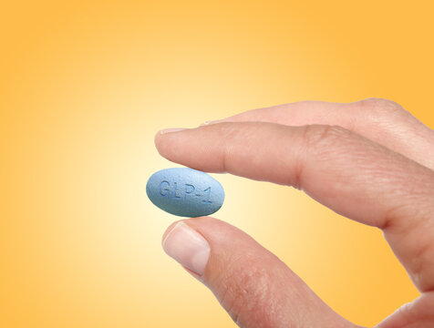 A woman's hand holding a GLP-1 pill on warm color background