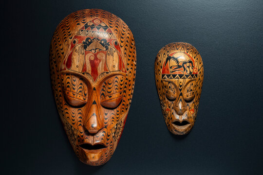 Pair of handcarved ethnic african wooden masks with intricate tribal patterns and geometric ornaments hanging on dark wall, closeup, ideal for interior decor, travel, and cultural concepts