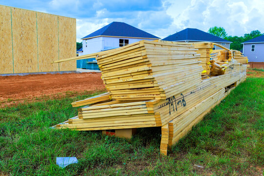 Wood beams planks are stacked neatly at construction site surrounded by homes be preparing for building.