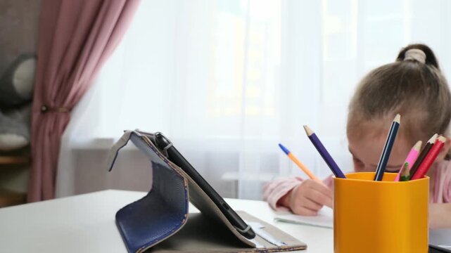 Child studying at home writing in notebook with modern online learning setup