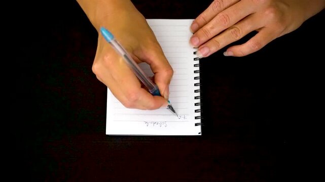 Top view of hand writing daily schedule in notebook on dark desk