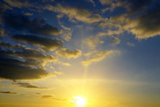 Majestic Sunrise Sky with Bright Sun Rays and Dramatic Fluffy Clouds. Beautiful Golden Light Illuminating Dark Blue Skyscape Background with Copy Space.