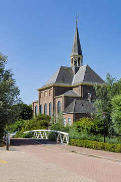 Alphen aan de Rijn, Netherlands - Exterior view of the historic Oudshoornse church built in 1665 with a wooden footbridge and lush greenery on a clear sunny summer day.
