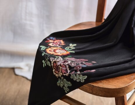 black fabric draped over a wooden chair shows delicate floral embroidery in soft colors calm elegant mood for fashion and home decor styling