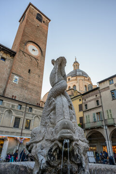 Baroque marble facade of Mantua cathedral with statues and romanesque bell tower at sunset, Italy