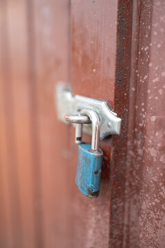 Close-up of a blue padlock securing a weathered metal latch on a wooden door, symbolizing security and protection