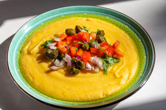 Traditional Greek fava yellow split pea puree garnished with capers diced tomatoes and red onion in a ceramic bowl