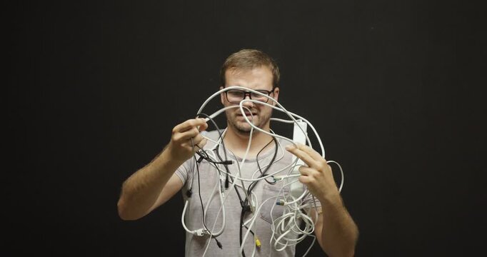 Frustrated man holding a tangled bundle of cables and electronic wires while trying to figure out how they work. Concept of technology confusion, cable management problems, and technical frustration 