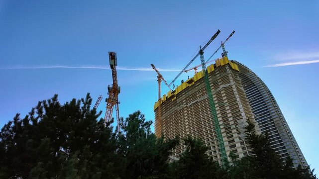 Timelapse of tower cranes working atop a rising high-rise building against a clear evening sky.
