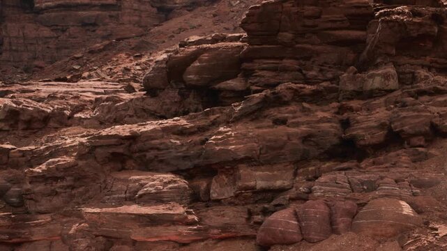 The scene shows a rugged landscape with large rock formations in a canyon. The sun shines down on the brown and red soil, creating shadows and highlights in the terrain.