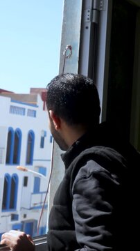 Young Thoughtful Man Looking Out of Window at City Street in Bright Morning Light