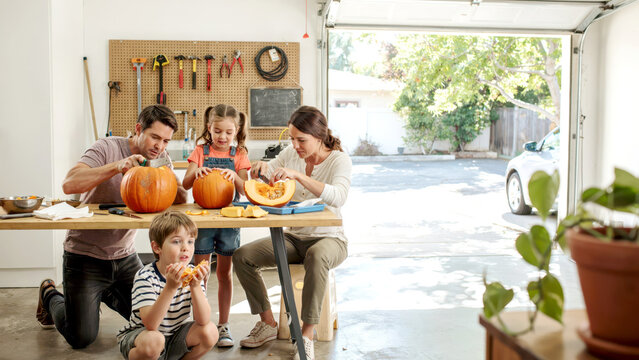 Family togetherness preparing seasonal pumpkins for decoration inside a bright open garage workspace environment with gathering around wooden