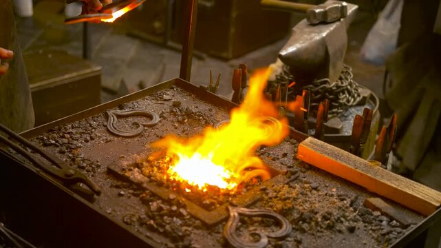 Blacksmith forging iron heart in workshop fire. Skillful blacksmith using tongs to heat a metal heart-shaped object in the hot embers of a forge, with bright orange flames and sparks flying