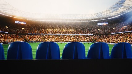 Empty blue stadium seats face a blurred soccer field as players wait for kickoff on match day, showing a quiet sports venue before the tournament action. © DC Studio