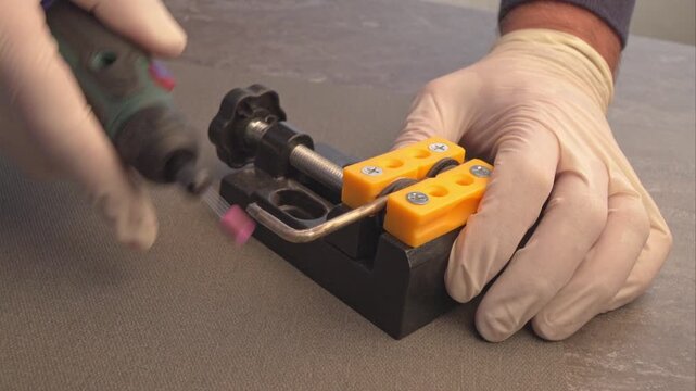 Precision metal grinding with rotary tool and bench vice close-up. craftsman wearing protective gloves while using a high-speed rotary tool with a grinding bit to process and shape 