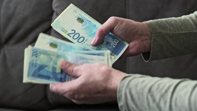 Male hands count Israeli new shekel banknotes in blue color with a 200 NIS denomination in a close-up view