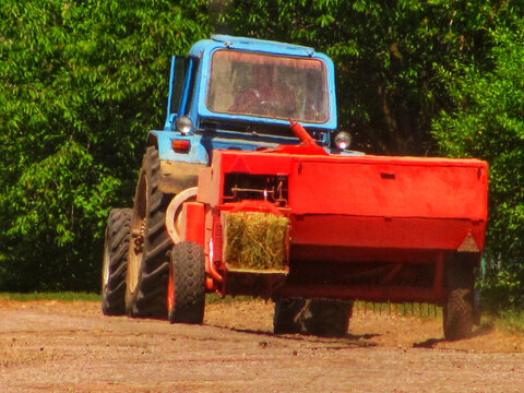 Blue tractor pulling a red square hay baler on a dirt country road