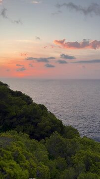 Scenic vertical sunrise view of Capdepera Lighthouse seen on coast of Mallorca, with calm sea illuminated by soft morning light. Seascape, travel