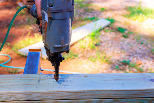 Carpenter uses air power tool to secure wooden boards on workbench outside.