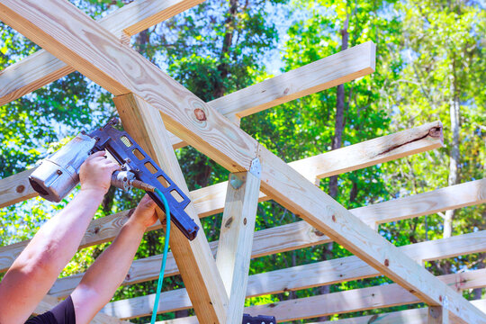 Contractor works on wooden beams frame using nail gun in clear outdoor area