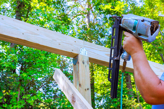 Contractor uses air nail gun to attach wood beams in backyard under work on construction project.