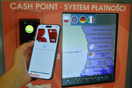 Close-up of a person holding a smartphone to make a contactless NFC mobile payment at a modern self-service laundry terminal.