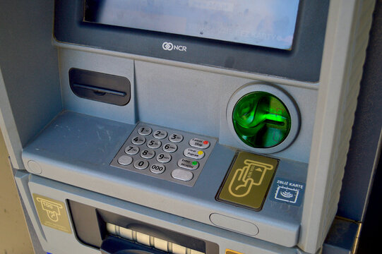 Close-up of a modern automated teller machine showing numeric keypad, illuminated green card slot, and contactless payment reader for automated banking transactions.