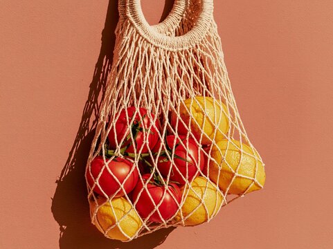Fresh tomatoes and lemons in a woven net bag hanging against a textured wall